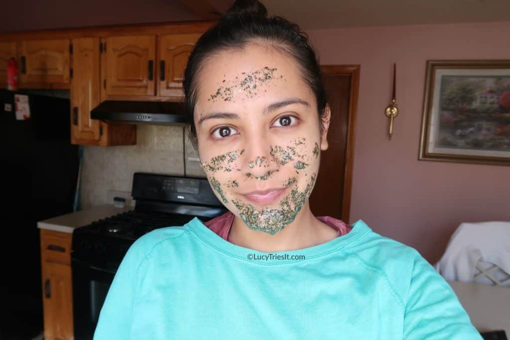 Young woman's face wearing a homemade green tea face mask for acne with her kitchen in the background.