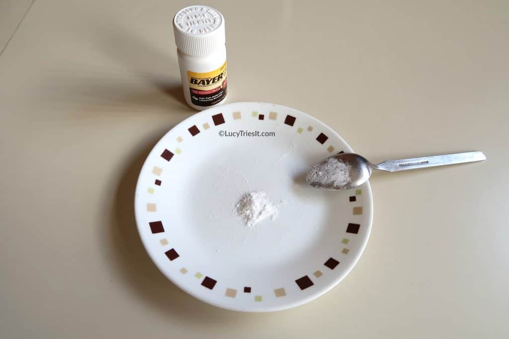 Crushed aspirin tablets on plate with spoon and aspirin container on the side.