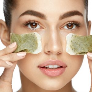 Young Woman With Natural Facial Makeup Holding Green Tea Bags On White Background for post about the green tea benefits for acne.